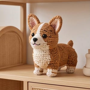 Può includere: Una statuetta di cane corgi all'uncinetto realizzata con filato marrone e bianco. Il peluche presenta grandi orecchie a punta, una striscia bianca che va dalla fronte al petto, occhi in plastica nera e un piccolo naso nero con bocca ricamata.