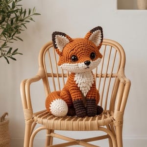 K&ouml;nnte beinhalten: Ein geh&auml;keltes Fuchs-Stofftier mit einem leuchtend orangefarbenen K&ouml;rper, einem wei&szlig;en Brustfleck und einer wei&szlig; gespitzten Rute. Der Fuchs hat dunkelbraune Ohren, dunkelbraune Pfoten und gro&szlig;e schwarze Sicherheitsaugen aus sichtbarem Garn.