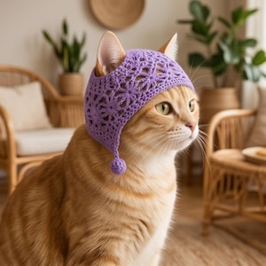 May include: A ginger cat wearing a light purple crocheted bonnet featuring a delicate floral pattern and a small pom-pom detail hanging from the side. The bonnet covers the top of the head and ears, showcasing intricate yarn work and texture.