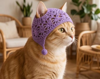 Könnte beinhalten: Eine ingwerfarbene Katze trägt eine hellviolette Häkelhaube mit einem zarten Blumenmuster und einem kleinen Bommel an der Seite. Die Haube bedeckt den Kopf und die Ohren und zeigt eine detaillierte und strukturierte Handarbeit aus Garn.