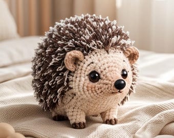 May include: A crocheted hedgehog stuffed animal featuring a cream-colored face and underbelly with a textured, dark brown and white spiky back. The toy has small rounded ears, a black nose, and large dark eyes with subtle pink blush on its cheeks.