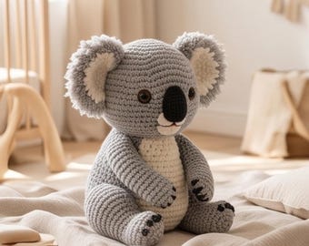 May include: A handmade crochet koala stuffed animal featuring a grey body with a cream-colored belly and inner ears. The koala has dark brown safety eyes, a black stitched nose, and small black claw details on its hands and feet, crafted in yarn.