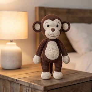 May include: A brown and cream-colored monkey doll crafted with a crochet technique. The monkey features a round head, large ears, a light-colored face and belly, and matching light-colored hands and feet, standing in an upright position.
