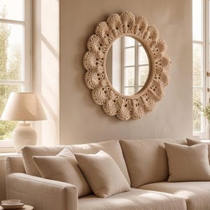 May include: A circular wall mirror featuring a decorative frame crafted with beige crochet work in a scalloped, petal-like pattern. The mirror has a smooth, reflective glass center surrounded by the textured, woven fiber border.