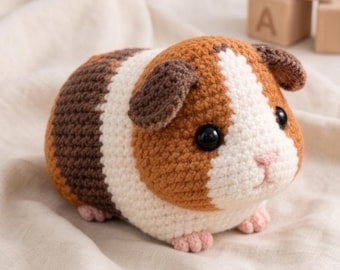Könnte beinhalten: Ein gehäkeltes Meerschweinchen-Stofftier mit einem dreifarbigen Muster aus braunem, weißem und dunkelbraunem Garn. Das Kuscheltier hat schwarze Sicherheitsaugen aus Kunststoff, eine kleine rosa gestickte Nase und winzige rosa gehäkelte Pfoten.