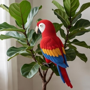 Puede incluir: Un loro de ganchillo hecho a mano con cabeza y cuerpo de color rojo vibrante, plumas alares medias de color amarillo brillante y plumas alares y de cola inferiores de color azul oscuro. El ave tiene una mancha blanca, pico beige y ojo gris.