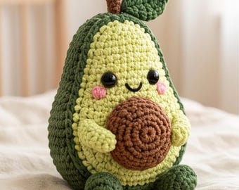 May include: A crocheted avocado plush toy featuring a dark green outer skin, a light green textured center, and a brown circular pit. The toy has two black plastic eyes, a stitched smile, and small pink cheeks, with a brown stem and green leaf on top.