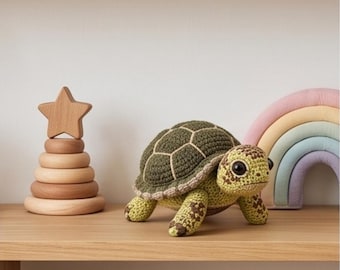 May include: A crocheted turtle toy featuring a dark olive green shell with light beige stitching, a light green head and limbs with brown spots, and large black eyes. The turtle is positioned on a wooden shelf next to a wooden star stacking toy.