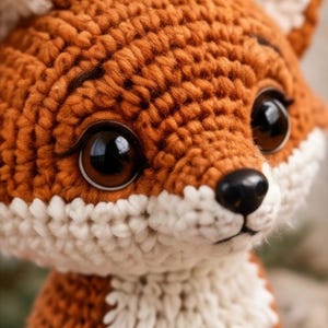 K&ouml;nnte beinhalten: Ein geh&auml;keltes Fuchskuscheltier mit leuchtend orangefarbenem Garn f&uuml;r Kopf und Ohren, kontrastiert durch cremewei&szlig;es Garn an Schnauze, Brust und Innenohren. Das Spielzeug hat gro&szlig;e, gl&auml;nzende dunkelbraune Sicherheitsaugen und eine kleine schwarze Nase.