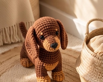 May include: A crocheted dachshund toy featuring a dark brown body with lighter tan accents on the paws, chest, and above the eyes. The stuffed animal has long floppy ears, a small black nose, and dark plastic eyes, crafted with visible yarn stitches.