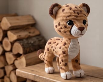 May include: A crochet stuffed animal shaped like a cheetah with tan yarn, dark brown spots, a white muzzle, and white paws. The toy features large black eyes, a brown nose, and rounded ears with dark brown accents, standing on four legs.