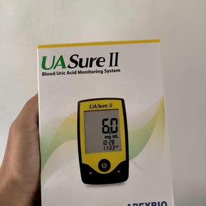 May include: A white box with the text "UA Sure II Blood Uric Acid Monitoring System" and a yellow and black blood uric acid monitor. The monitor displays a reading of 6.0 mg/dL. The box is labeled "BASIC KIT Suitable For Self-testing."