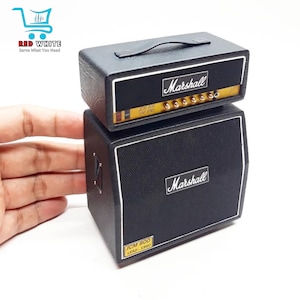 Könnte beinhalten: Ein Miniatur-Marshall-Verstärkerstapel in Schwarz. Der obere Verstärkerkopf hat einen Griff und das Marshall-Logo. Die untere Box hat einen Lautsprechergrill und das Marshall-Logo. Der Text "JCM 800 LEAD - 1960" ist auf beiden Teilen sichtbar.