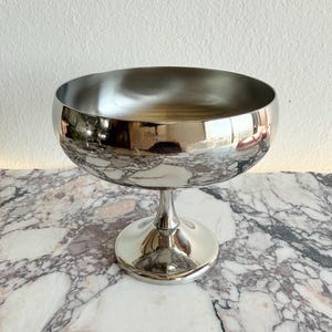 Peut inclure: Une coupe à champagne en métal argenté brillant, avec un large bol et une fine tige. La coupe est posée sur une surface en marbre. Le bol reflète l'environnement.