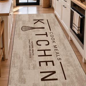 Puede incluir: Una alfombra de cocina rectangular con un fondo texturizado en tonos beige y crema desgastados. La alfombra presenta texto en marrón oscuro que dice KITCHEN, COOK MEALS y NATURAL HEALTH SWEET AND DELICIOUS, junto a un gráfico de un batidor.