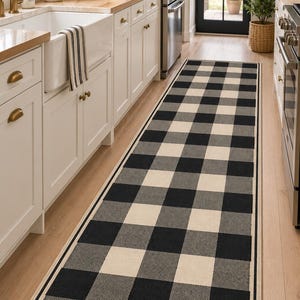 May include: A long, rectangular runner rug featuring a black and off-white buffalo check pattern. The rug has a solid black border framing the checkered design and is positioned on a light-colored wooden floor in a kitchen setting.