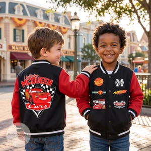 May include: A black and red varsity jacket featuring Lightning McQueen graphics. The back displays a large red race car with checkered flags and text. The front includes patches with the text RUSTEZE, MASON, 95, and Lightning McQueen.