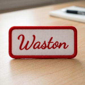 May include: A rectangular embroidered patch with a white fabric center and a thick red border. The word Waston is stitched in red cursive script across the center of the white background. The patch has rounded corners and a clean, finished edge.