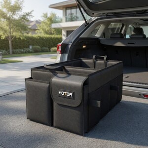 May include: Black car trunk organizer with multiple compartments and pockets. The organizer has a rectangular shape with a handle and the word "HOTOR" on the front. It is placed inside the open trunk of a gray car.