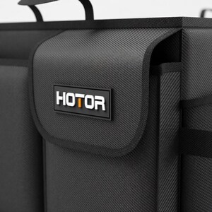 May include: Black storage organizer with the word "HOTOR" in white letters on a black rectangular patch. The organizer has a textured surface and a handle. The overall design is sleek and modern.