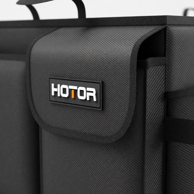 May include: Black storage organizer with the word "HOTOR" in white letters on a black rectangular patch. The organizer has a textured surface and a handle. The overall design is sleek and modern.