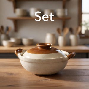 May include: A ceramic cooking pot with a lid, featuring a two-tone design of cream and brown. The pot has two handles and sits on a wooden surface. The word "Set" is visible in the background.