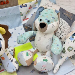 Può includere: Un giocattolo di peluche a forma di coniglio fatto a mano con orecchie e arti in tessuto a fantasia blu e bianco. Il coniglio ha un viso beige e un naso nero. Il giocattolo è circondato da altri giocattoli fatti a mano e da una trapunta patchwork con vari motivi e colori.