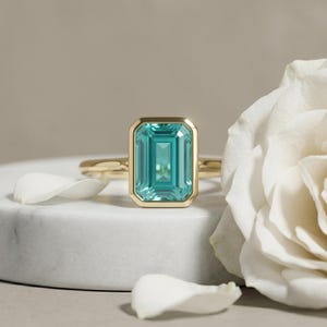Anillo de compromiso con gema de turmalina verde azulada talla esmeralda y engaste biselado.