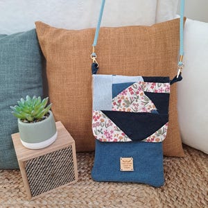 May include: A patchwork crossbody bag with a light blue strap and gold-colored hardware. The bag features denim and floral fabric panels. A small, rectangular tag is sewn on the front.