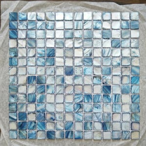 May include: A square sheet of mosaic tiles featuring a pattern of small, square tiles in shades of blue and white. The tiles have a glossy finish, creating a reflective surface. The overall effect is reminiscent of water or a cloudy sky.