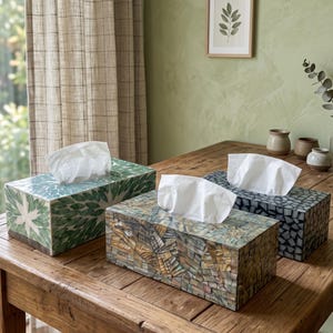 Puede incluir: Tres cajas rectangulares para pañuelos con diseños de mosaico. Una es verde con un patrón de hojas, otra es marrón e iridiscente con un mosaico geométrico, y la tercera es gris oscuro con un patrón de pequeñas piezas irregulares.