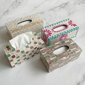 May include: Four rectangular tissue box covers featuring mosaic tile patterns. One has cream-coloured scales, one has a teal and magenta floral design, one has a grid of white, green, and maroon squares, and one has a brown and green brick-like pattern.