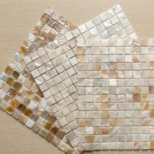 May include: Three mosaic tile sheets in shades of white, beige, and brown. Each sheet is made up of small, square tiles arranged in a grid. The tiles have a pearlescent sheen, reflecting light and creating a textured appearance. The tiles are approximately 1 cm square.