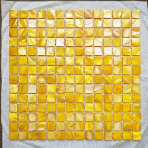 Puede incluir: Una lámina cuadrada de baldosas de mosaico. Las baldosas son pequeñas, cuadradas y una mezcla de amarillo y blanco. Las baldosas tienen un brillo nacarado, lo que les da un aspecto brillante. El mosaico está sobre una hoja de papel blanco.