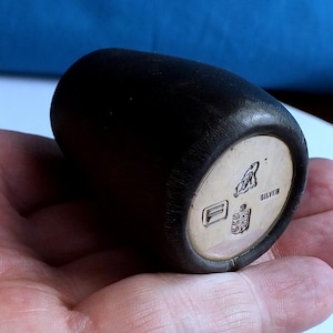 Puede incluir: Un objeto cilíndrico negro con una base plateada. La base plateada tiene un diseño en relieve y la palabra "SILVER". El objeto se sostiene en una mano.
