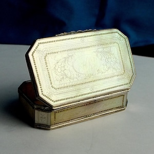 May include: An open, antique silver box with an octagonal lid. The lid is engraved with floral and scroll designs, and the box has a hinged opening. The box is likely made of sterling silver.