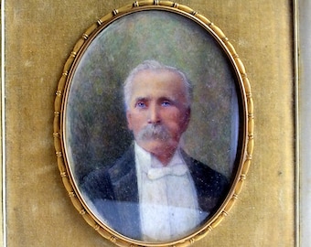 May include: An oval portrait painting of an older individual with gray hair and a mustache, wearing a dark jacket, white shirt, and white bow tie. The portrait is encased in a decorative gold-toned metal frame with a textured, beaded edge detail.