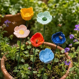 May include: A selection of colourful, handmade flower garden stakes in a terracotta pot. The flowers are painted in shades of yellow, pink, red, blue, and green, with green stems. Bees are seen near the flowers. The garden stakes add a decorative touch to any garden.