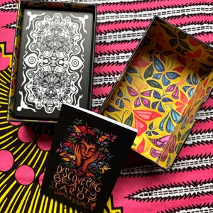 May include: A tarot card set with a black box featuring a white floral design and a yellow box with a butterfly pattern. The set includes a black booklet titled "Discovering Beauty Tarot" by Sophia Litwak.