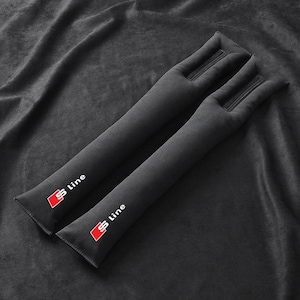 May include: Two black seat belt shoulder pads with the "S Line" logo in red and white. The pads are made of a soft material and have a rectangular shape with a zipper detail at the top. The background is a dark gray fabric.