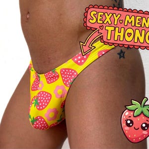 Könnte beinhalten: Ein gelber Tanga mit einem sich wiederholenden Muster aus roten Erdbeeren mit weißen Kernen und kleinen rosa Blumen. Das Bild enthält ein grafisches Textfeld mit der Aufschrift SEXY MEN'S THONG, einem Pfeil zum Kleidungsstück und einem Erdbeersymbol.