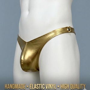 May include: Gold-coloured thong underwear made of elastic vinyl. The underwear has a V-shaped front and a thin waistband with a button closure on the side. The text "HANDMADE • ELASTIC VINYL • HIGH QUALITY" is visible at the bottom.