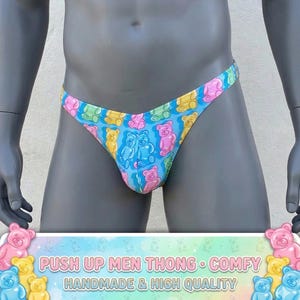 May include: A blue thong featuring a repeating pattern of colourful gummy bear illustrations. The bears are pink, yellow, and blue. The text at the bottom reads "PUSH UP MEN THONG • COMFY HANDMADE & HIGH QUALITY".