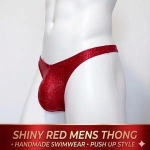 May include: Shiny red thong swimsuit with a textured, shimmering appearance. The swimwear is displayed on a white mannequin. The text at the bottom reads "SHINY RED MENS THONG - HANDMADE SWIMWEAR - PUSH UP STYLE".