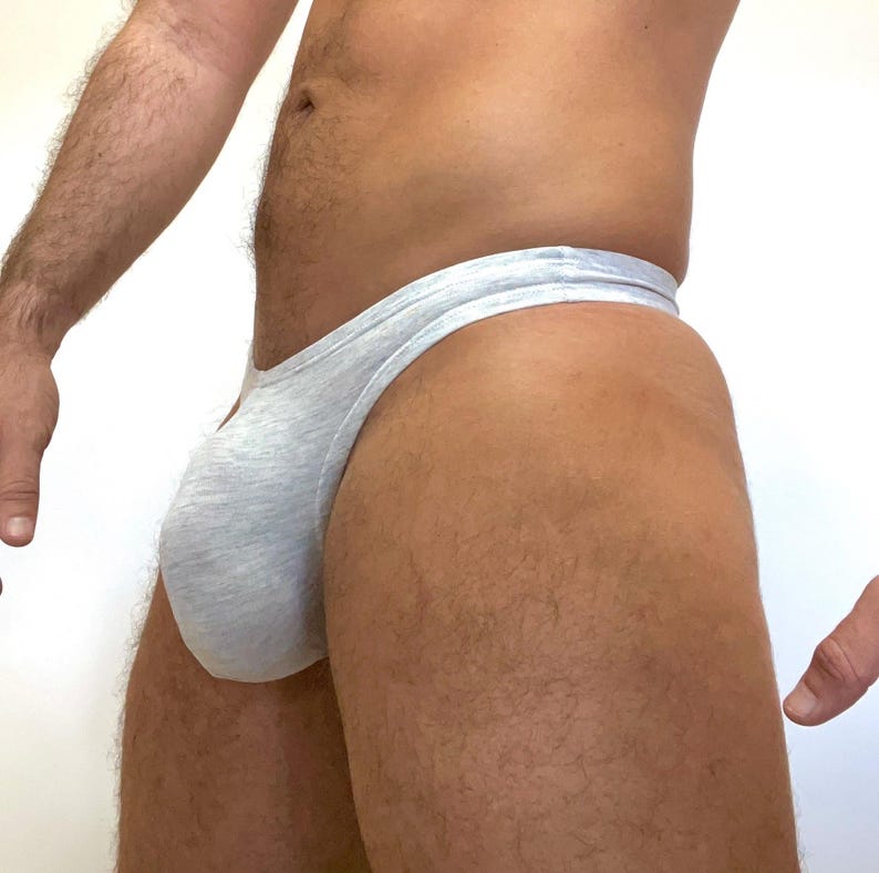 May include: Light grey thong underwear made from a soft, stretchy fabric. The image shows a side view of the underwear.