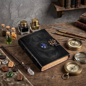 Könnte beinhalten: Ein schwarzes, ledergebundenes Notizbuch mit geprägten Halbmondmotiven und einem blauen Edelsteinverschluss. Das Bild zeigt auch Tintenfässer, einen Kompass, einen Zauberstab und kleine Glasflaschen, die ein mystisches Thema schaffen.