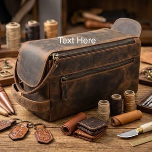 Può includere: Una borsa da viaggio in pelle marrone con più cerniere e un manico. La borsa è circondata da strumenti per la lavorazione della pelle, tra cui rocchetti di filo, portachiavi e un piccolo coltello. Il testo "Text Here" è visibile sulla borsa.