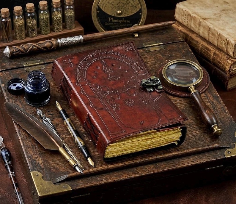May include: A vintage-style leather-bound journal with embossed tree and star designs, a magnifying glass, and various writing tools. The scene includes ink bottles, quills, and pens, all arranged on a wooden box.