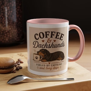 Könnte beinhalten: Weiße Keramik-Tasse mit rosa Innenraum und Henkel, mit dem Text "Coffee & Dachshunds" und einer Illustration eines Dackels mit einer Kaffeetasse. Die Tasse steht auf einer Holzoberfläche.