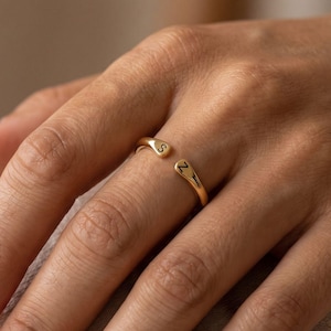 Peut inclure: Une bague ouverte dorée avec deux extrémités arrondies, chacune gravée d'une lettre noire. Une extrémité porte la lettre S, tandis que l'autre extrémité porte la lettre Z. L'anneau présente une finition lisse et polie avec un design ouvert réglable.